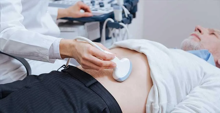 A man is having an abdominal ultrasound examination in London. The sonographer is holding a probe over his abdomenwith one hand and the other hand is resting on the ultrasound scanner.